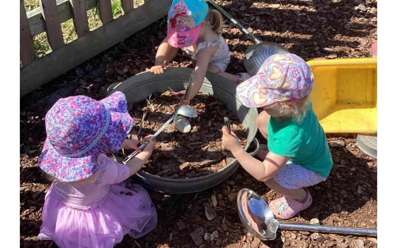 Three children playing outside with big spoons