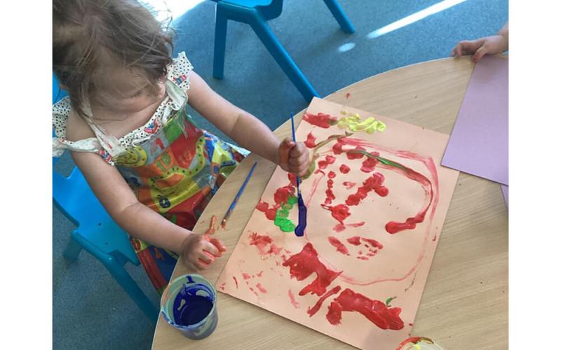 Child sitting at a table painting with red, green, yellow and blue paints