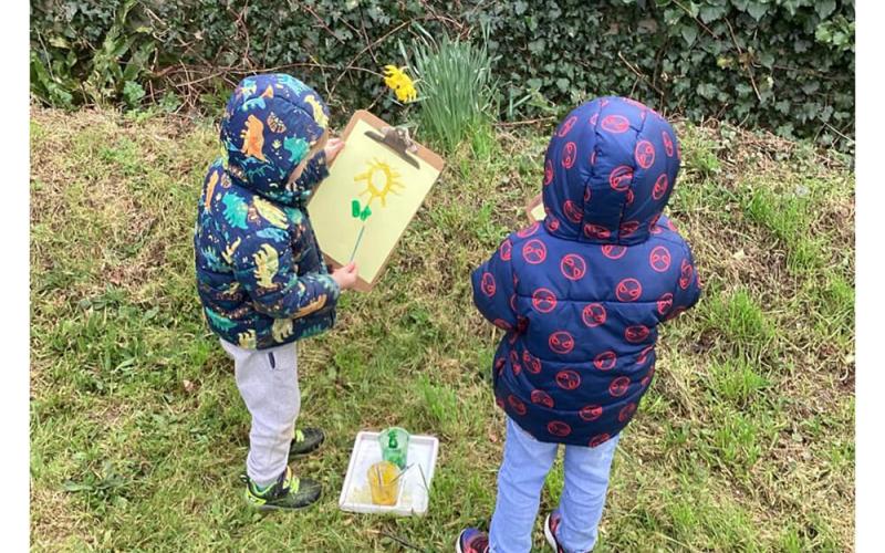Children painting a flower that they are looking at outside