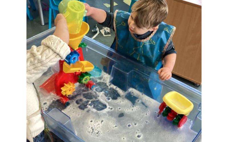 Children playing with water wheels in a large tray of soapy water